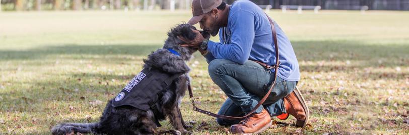 man kneeling kissing snout of service dog